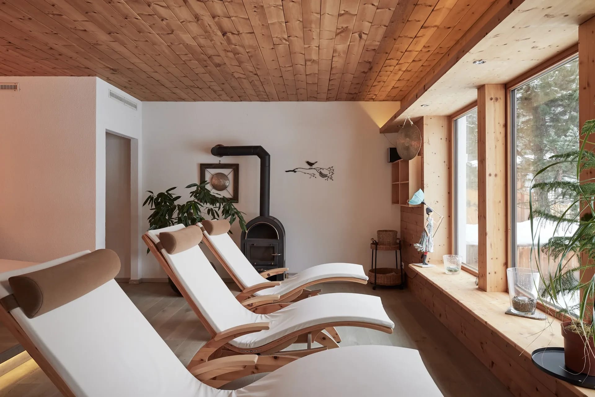 Ruheraum mit Liegen, Holzdecke und Kaminofen vor dem Fenster