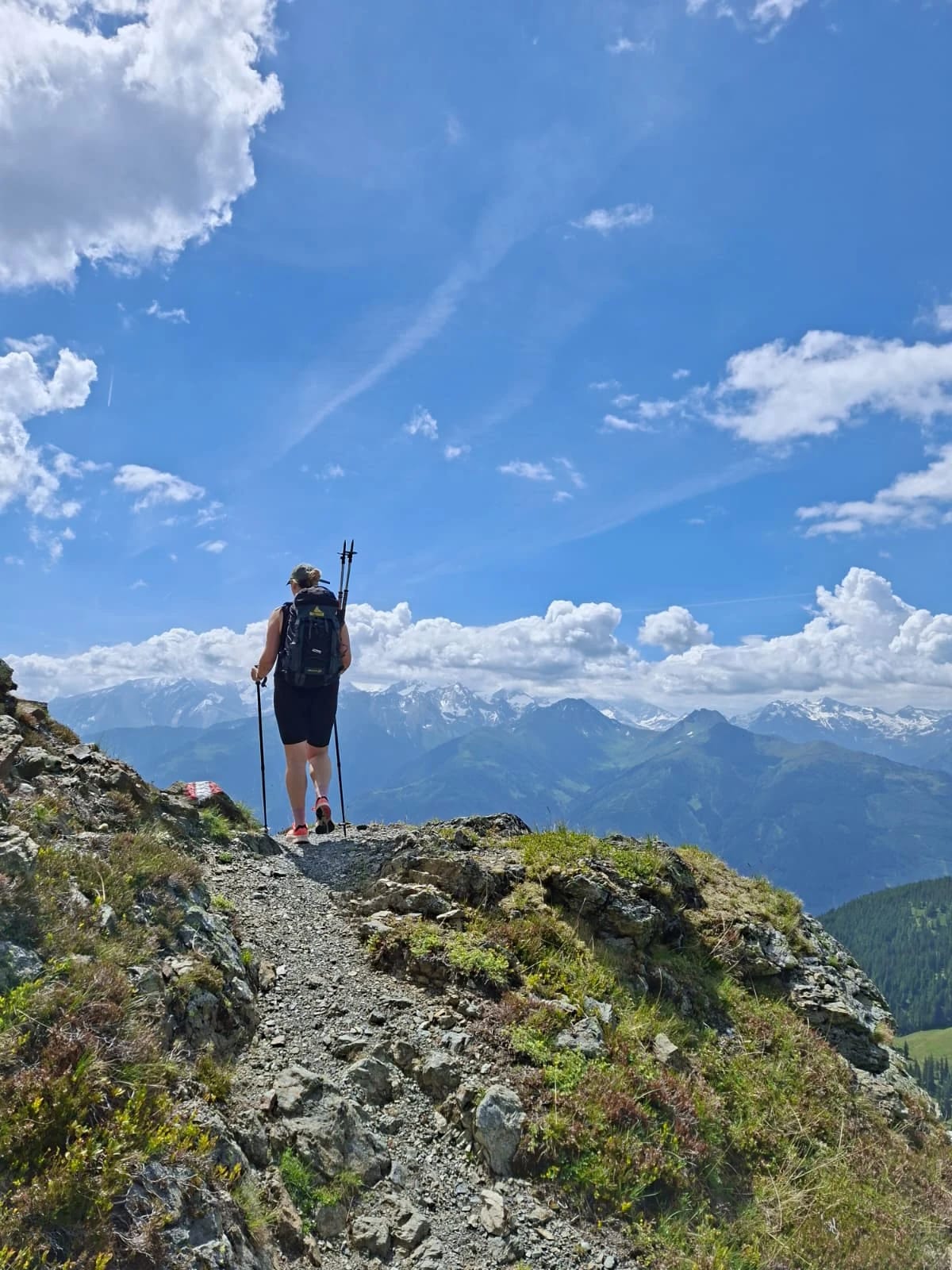 Person mit Rucksack und Trekkingstöcken auf einem schmalen Bergpfad