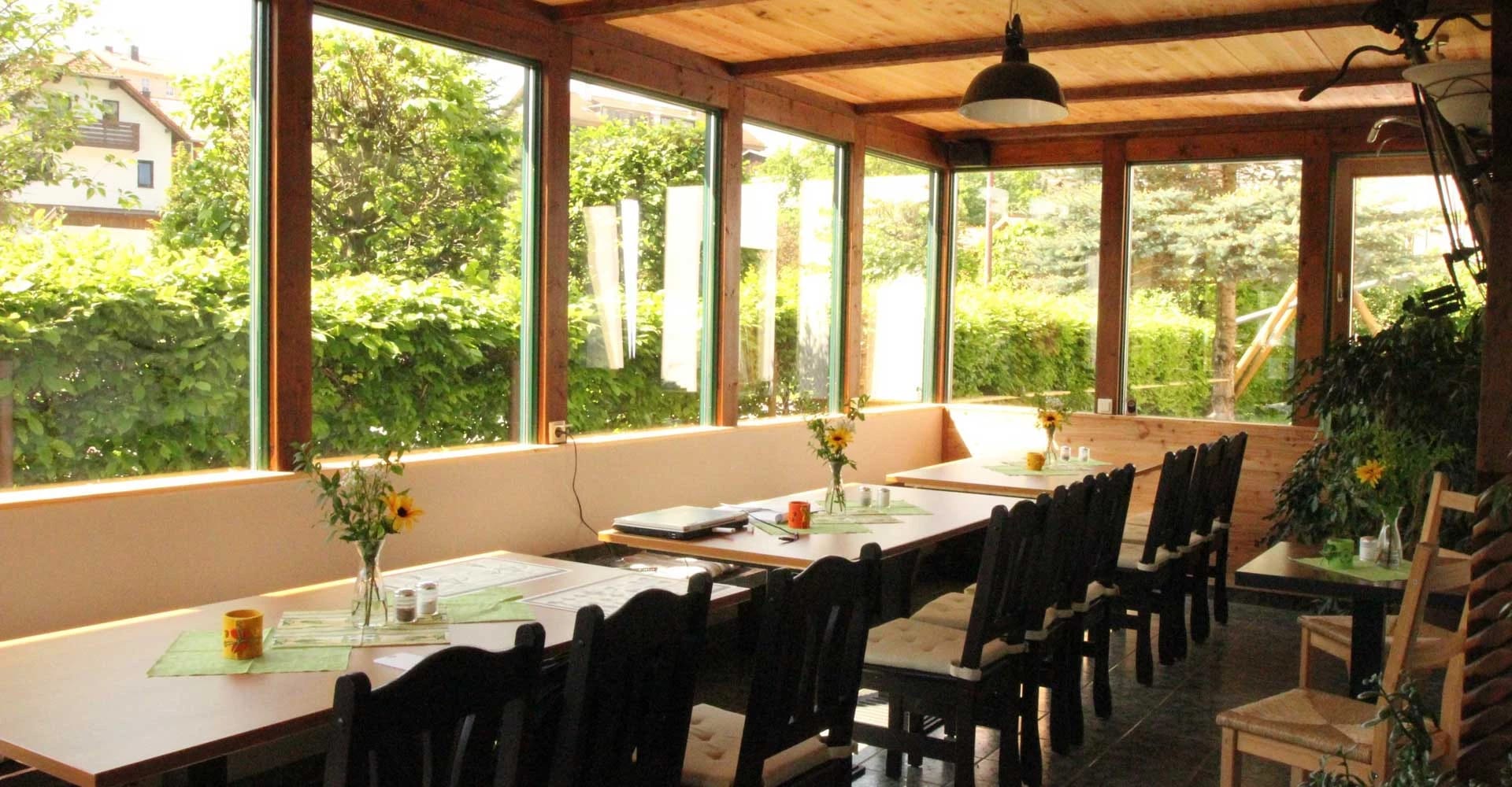 Wintergarten mit langer Tafel, Holzbank und umlaufender Fensterfront mit Blick in den Garten