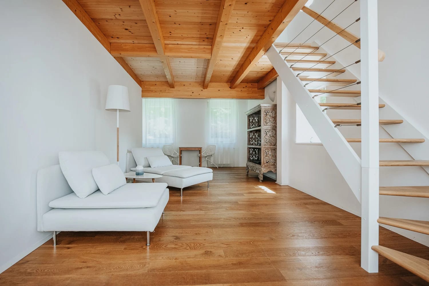 Wohnraum einer Ferienwohnung mit weißem Sofa, Holzdecke und Treppe