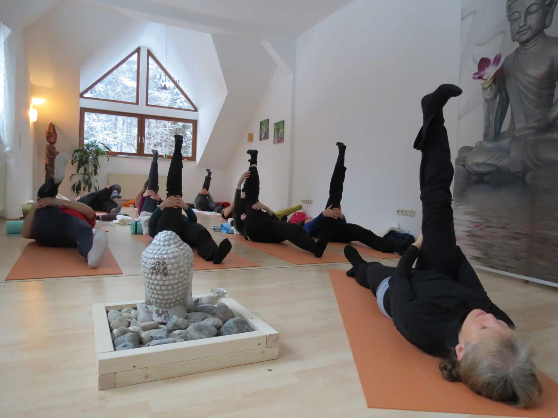 Heller Yogaraum unter dem Dach mit orangefarbenen Matten, Giebelfenster und Steinbrunnen