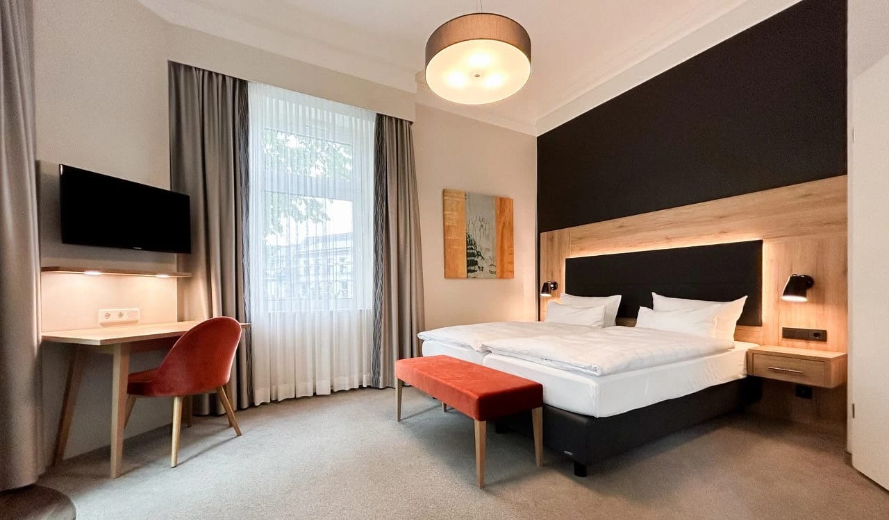 Modernes Zimmer mit hellem Holzkopfteil, dunkler Akzentwand, roter Bank am Bettende und Schreibtisch