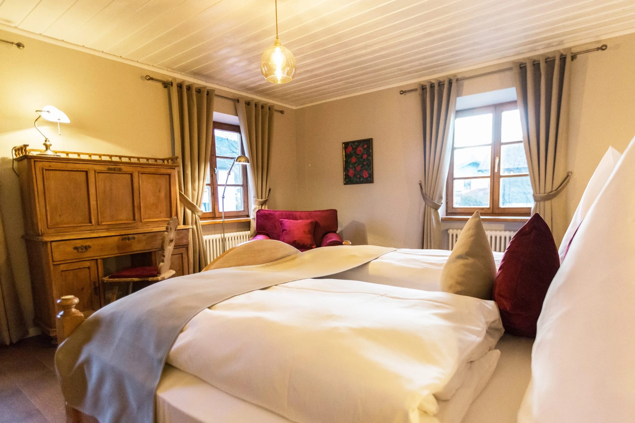 Doppelzimmer mit Holzbett, roten Kissen und zwei Fenstern