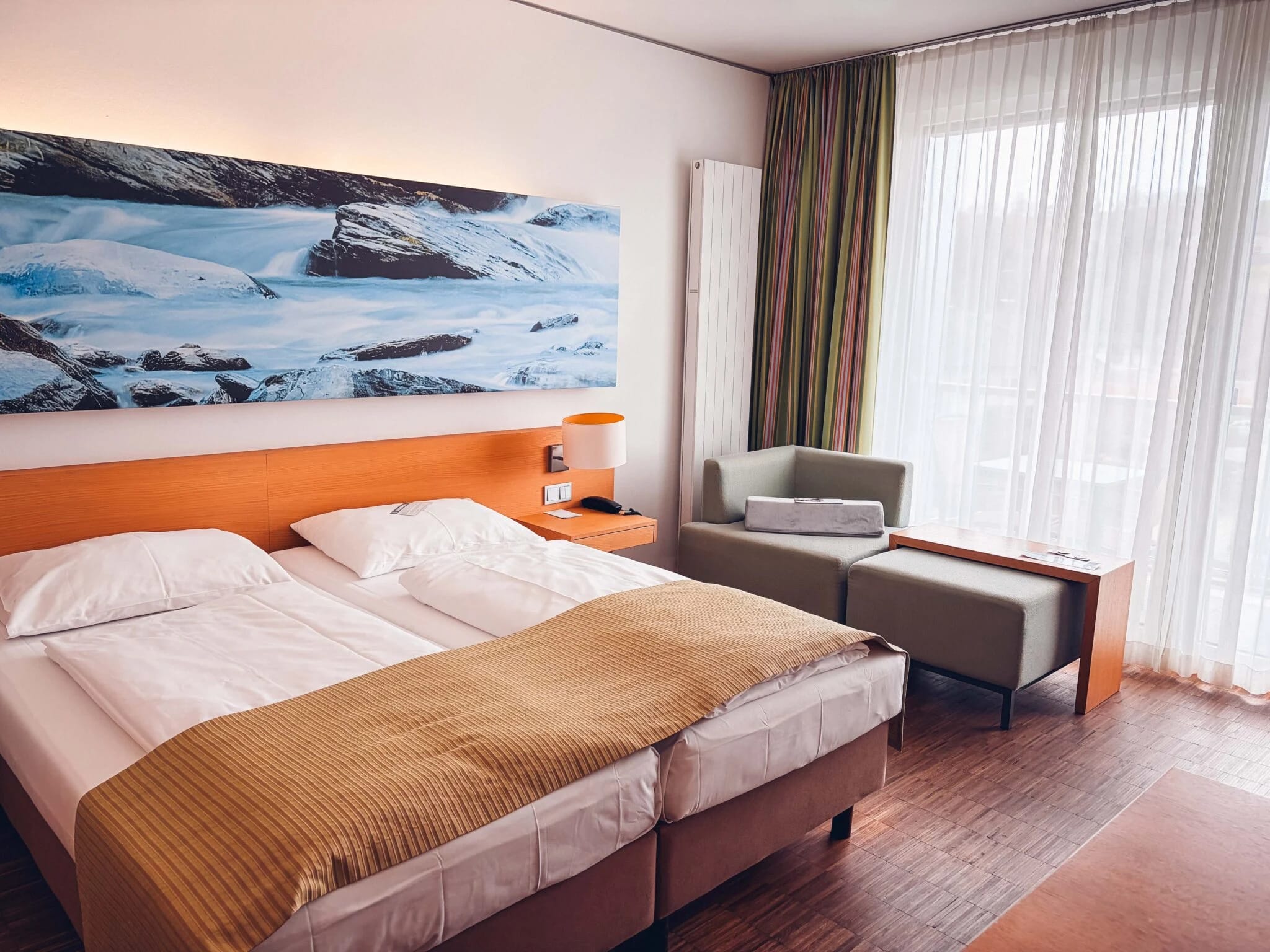 Helles Doppelzimmer mit Sessel, Hocker und bodentiefer Fenstertür zum Balkon