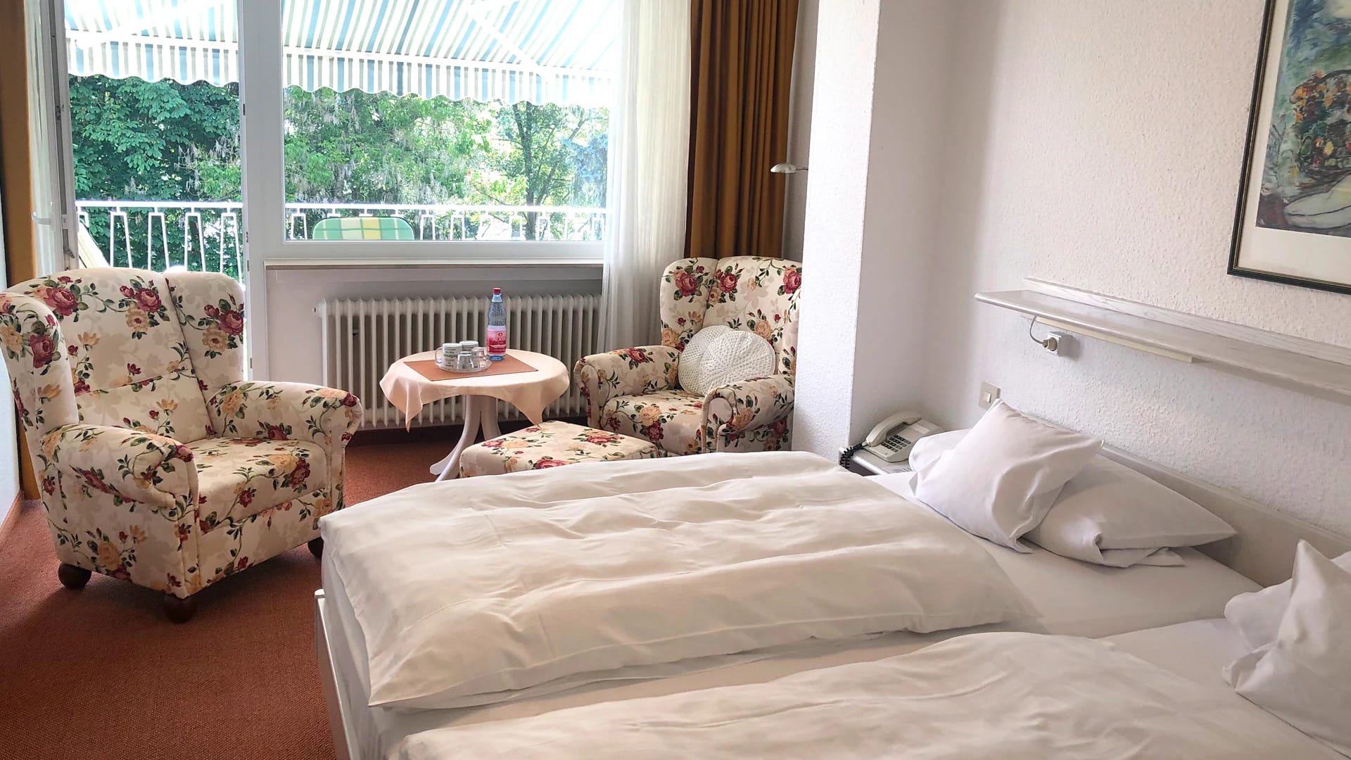 Zimmer mit Doppelbett, geblümten Sesseln und Balkon