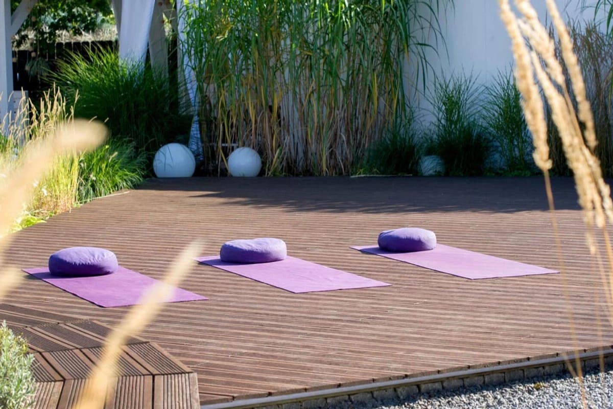 Yogamatten und Meditationskissen auf einer Terrasse im Grünen