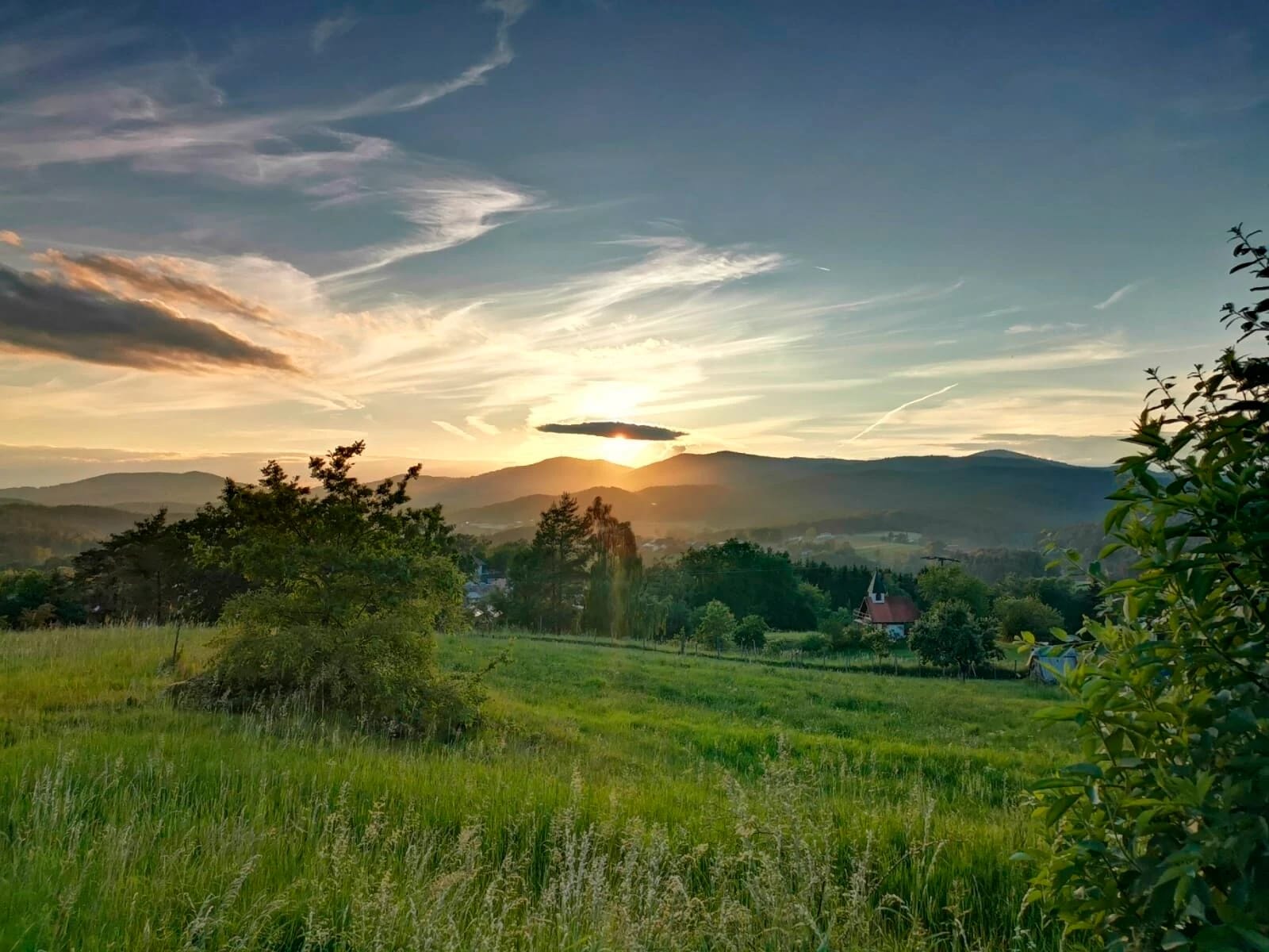 Sonnenuntergang über Wiesen und bewaldeten Bergkämmen