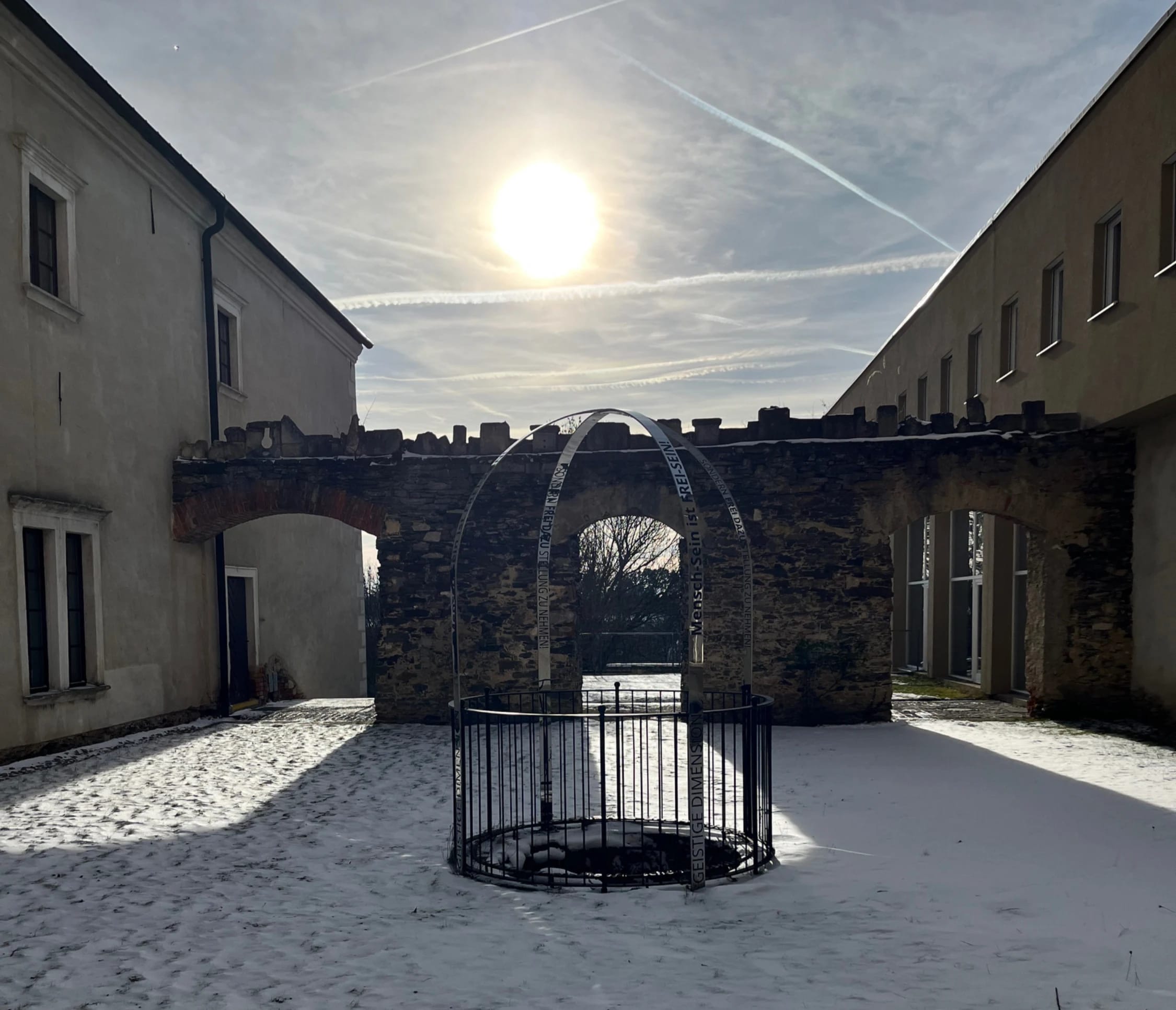 Historischer Innenhof im Winter mit überdachtem Brunnen und tiefstehender Sonne
