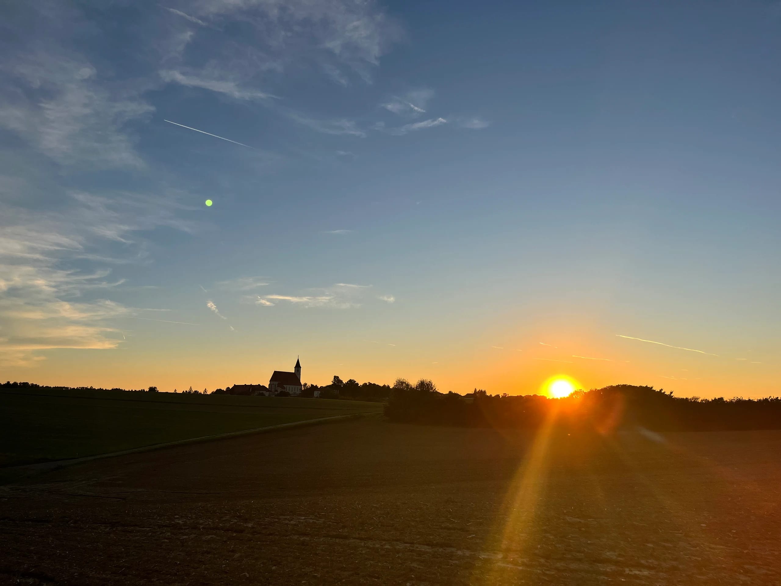 Sonnenuntergang über Feldern mit einer Kirche am Horizont
