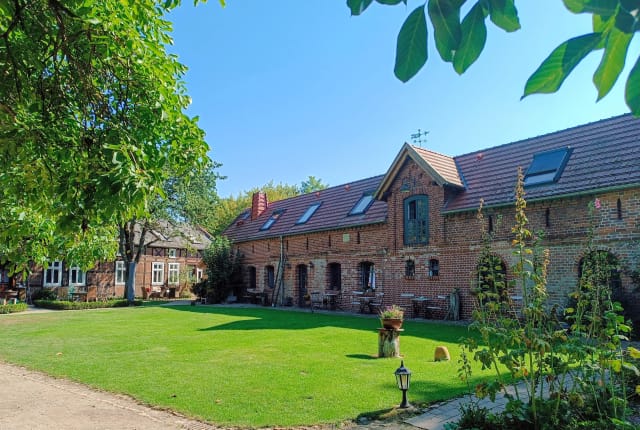 Innenhof des Deichhofs mit langem Backsteinhaus, Dachgauben und großer Rasenfläche unter blauem Himmel