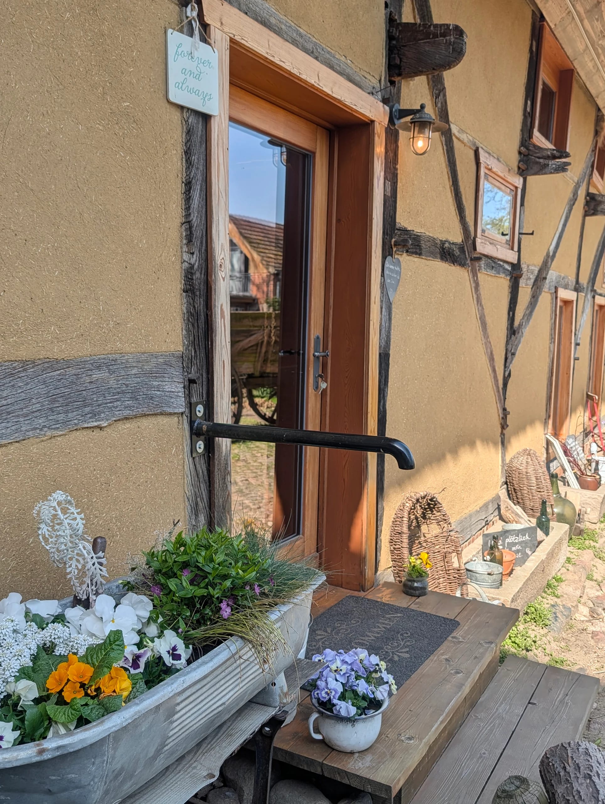 Hauseingang mit Holztür, Blumenkästen und bepflanzter Zinkwanne