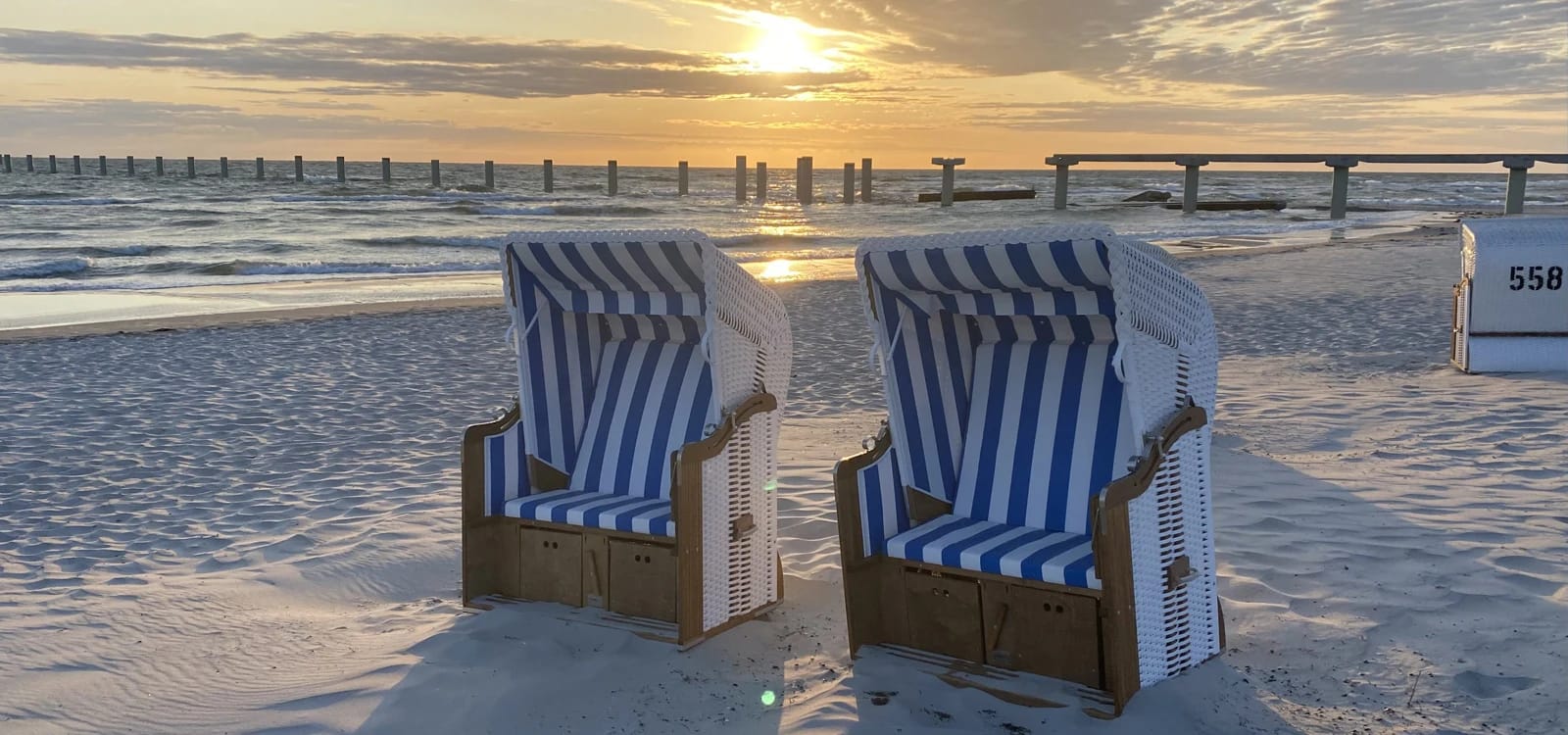 Strandkörbe am Ostseestrand bei Sonnenuntergang mit Seebrücke
