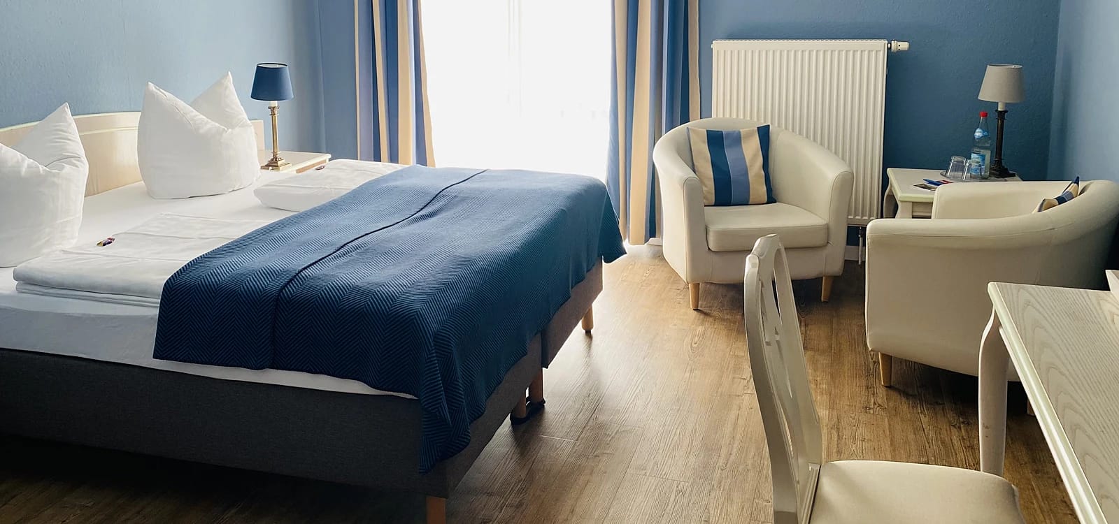 Zimmer mit Doppelbett und zwei weißen Sesseln vor blauer Wand
