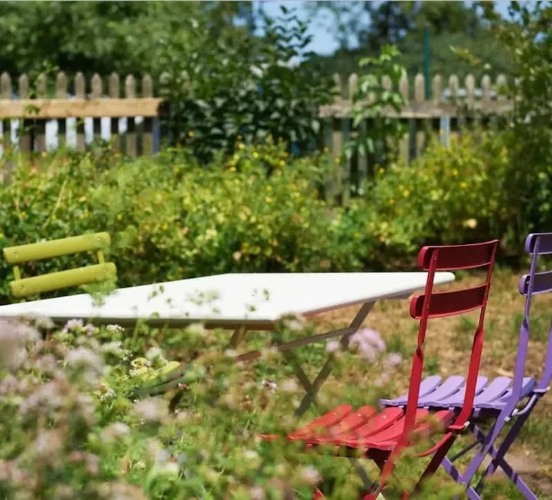Gartenplatz mit weißem Tisch und bunten Stühlen zwischen blühenden Beeten