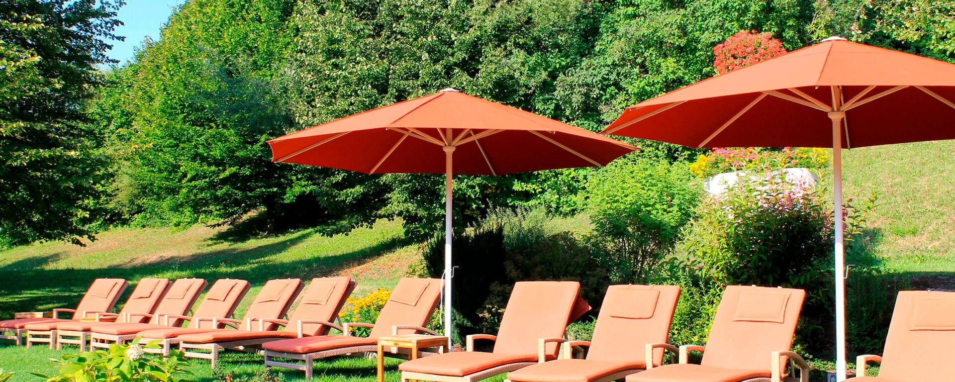 Liegestühle unter roten Sonnenschirmen auf der Liegewiese im Hotelgarten