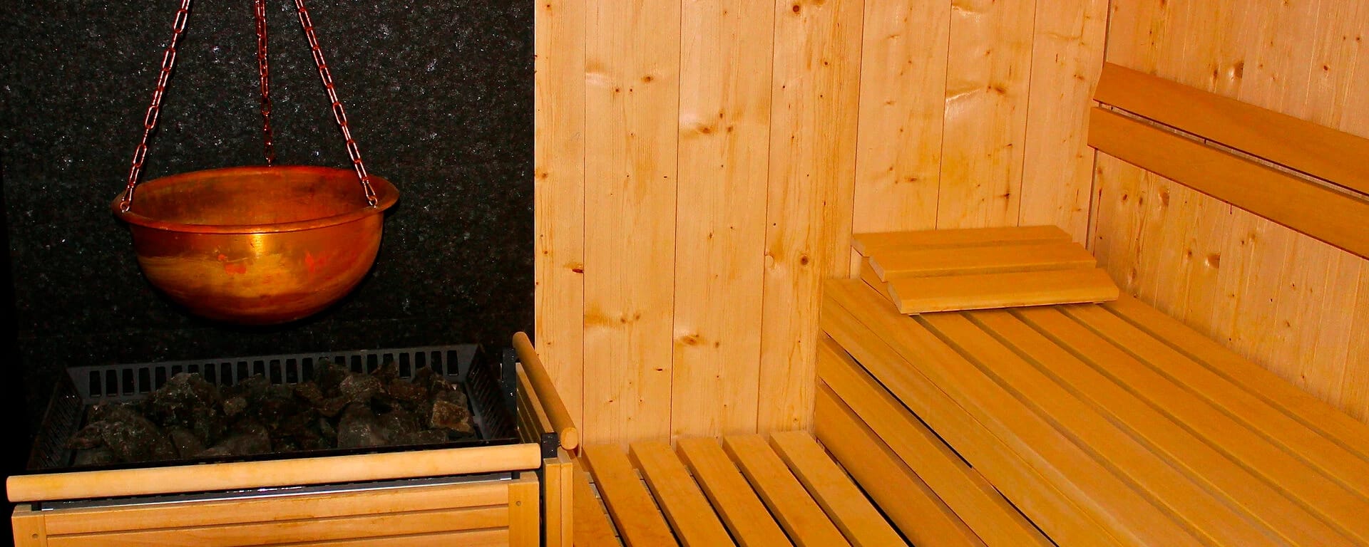 Finnische Sauna mit hellen Holzbänken, Saunaofen und Kupferkübel
