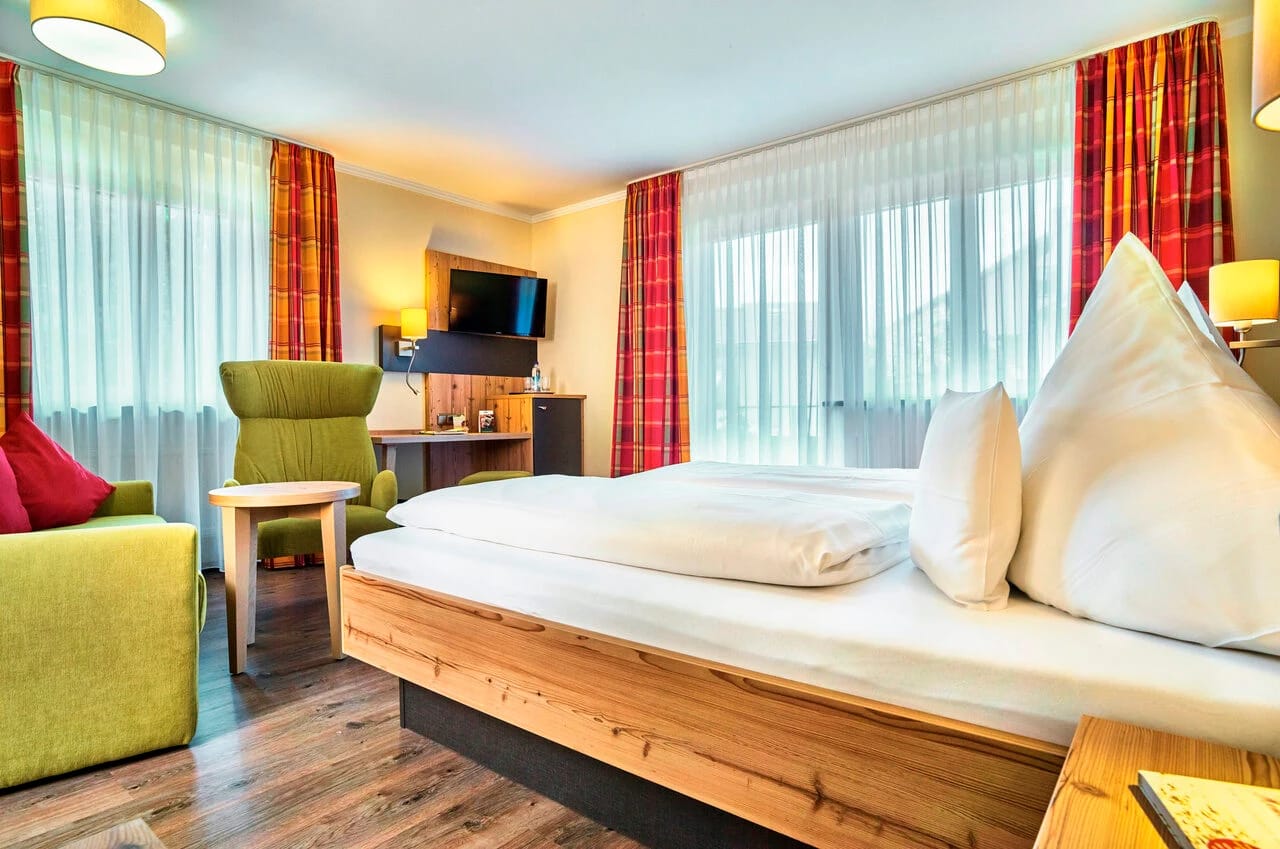 Doppelzimmer mit Holzbett, grünem Sessel und roten Vorhängen