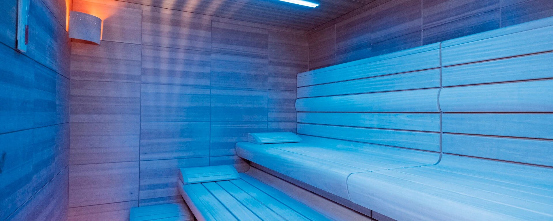 Biosauna mit hellen Holzbänken und blauer Beleuchtung