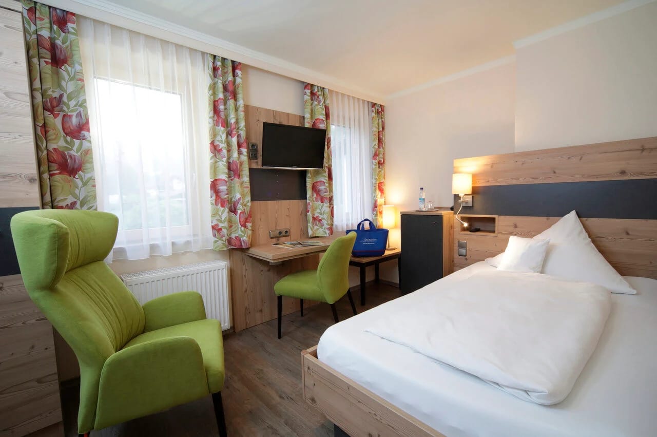 Modernes Doppelzimmer mit Holzelementen, grünen Sesseln und Schreibtisch