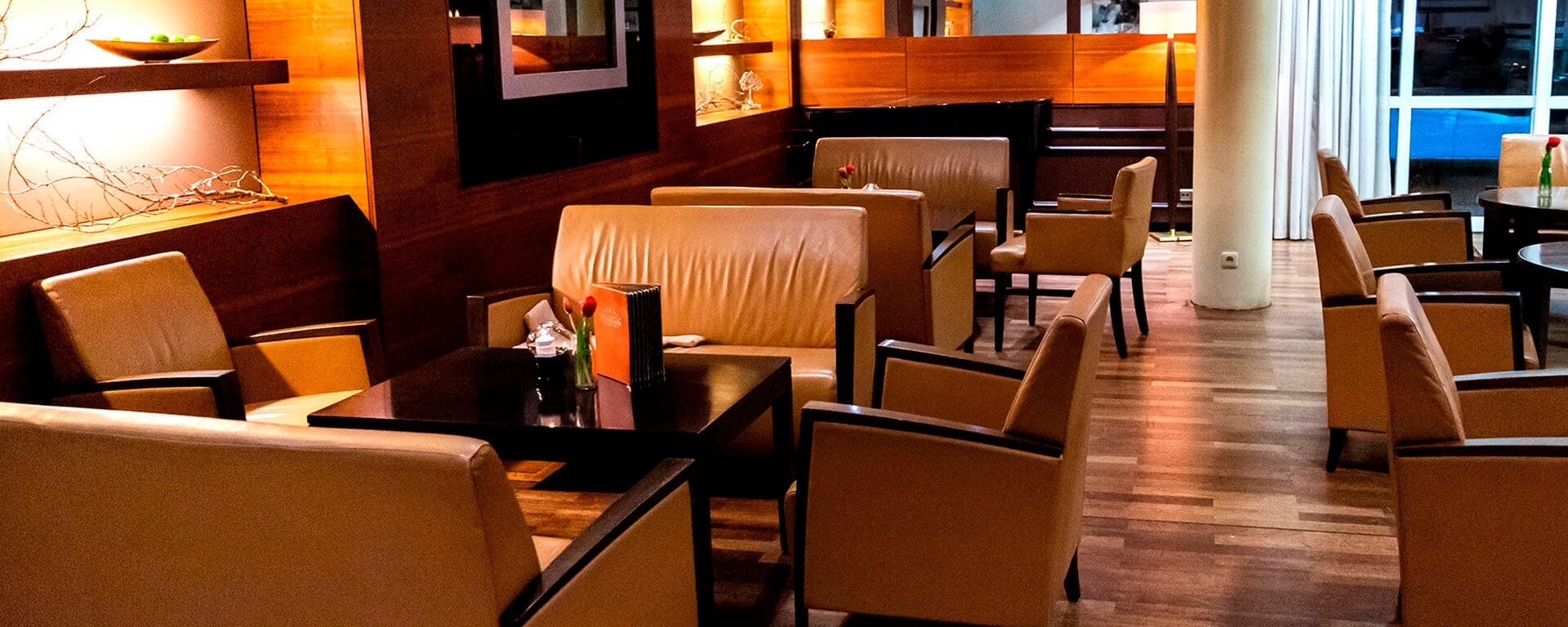 Loungebereich mit Ledersesseln, dunklen Holztischen und Wandvertäfelung