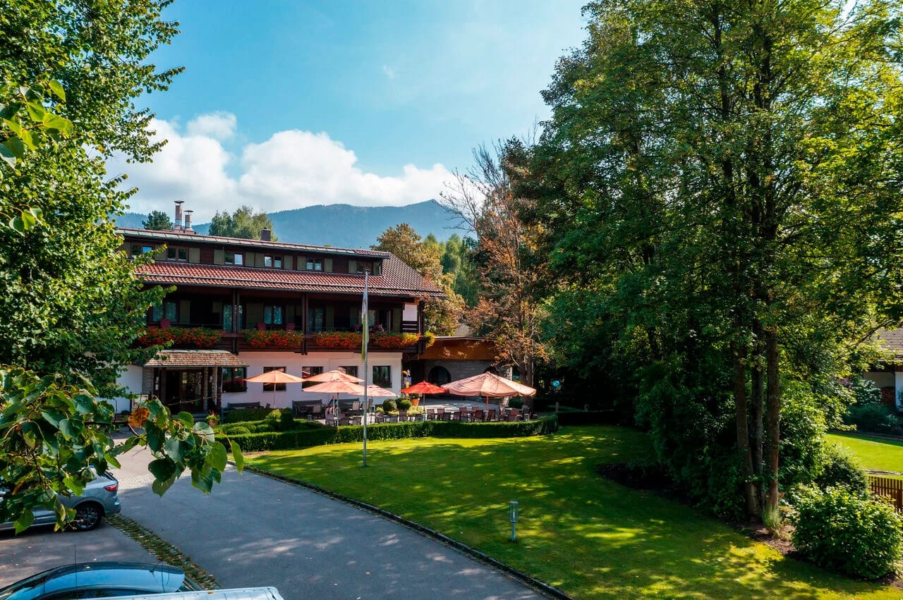 Das Hotelgebäude mit Gartenanlage und bewaldetem Berg im Hintergrund
