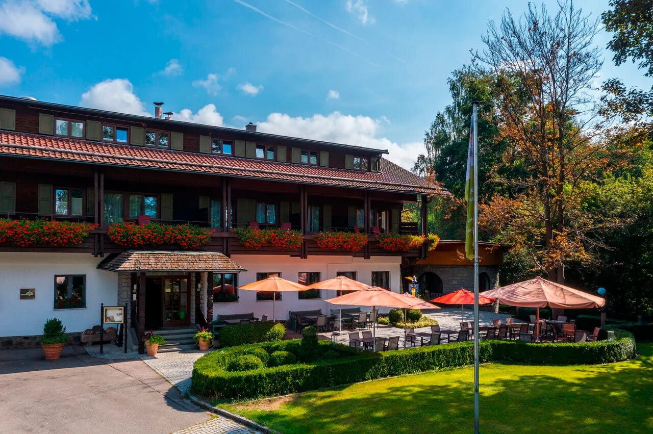 Außenansicht des Hotels mit Terrasse, Sonnenschirmen und Gartenanlage bei blauem Himmel