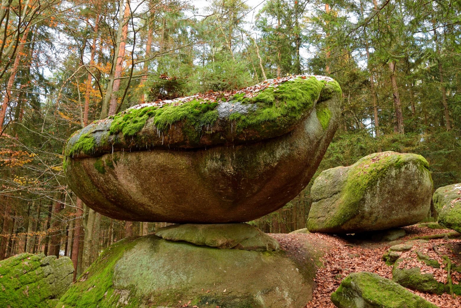 Der Wackelstein, ein großer moosbewachsener Felsblock auf Steinen im Wald