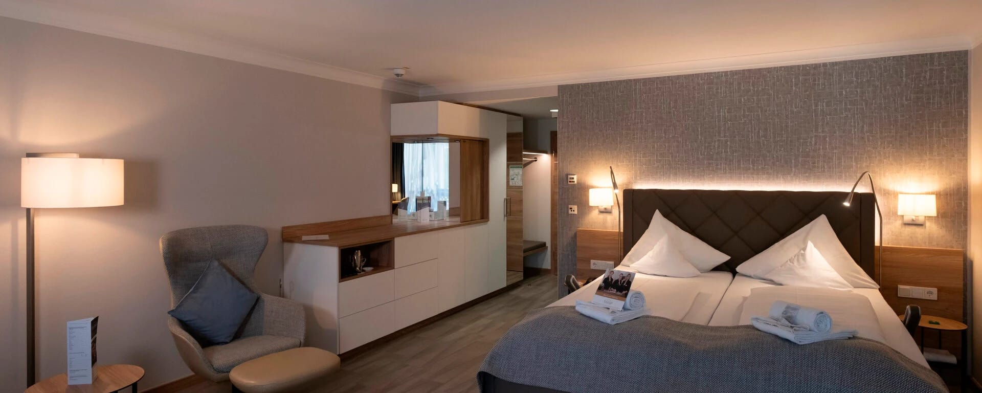 Geräumiges Hotelzimmer mit Doppelbett, Sessel mit Hocker und Sideboard