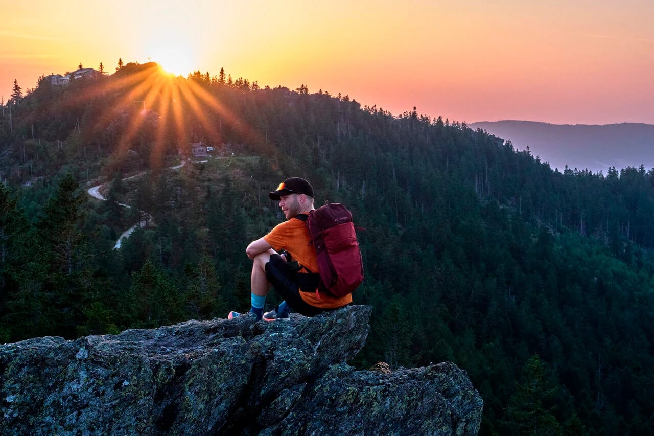 Wanderer auf einem Felsen mit Blick über die bewaldeten Hügel bei Sonnenuntergang