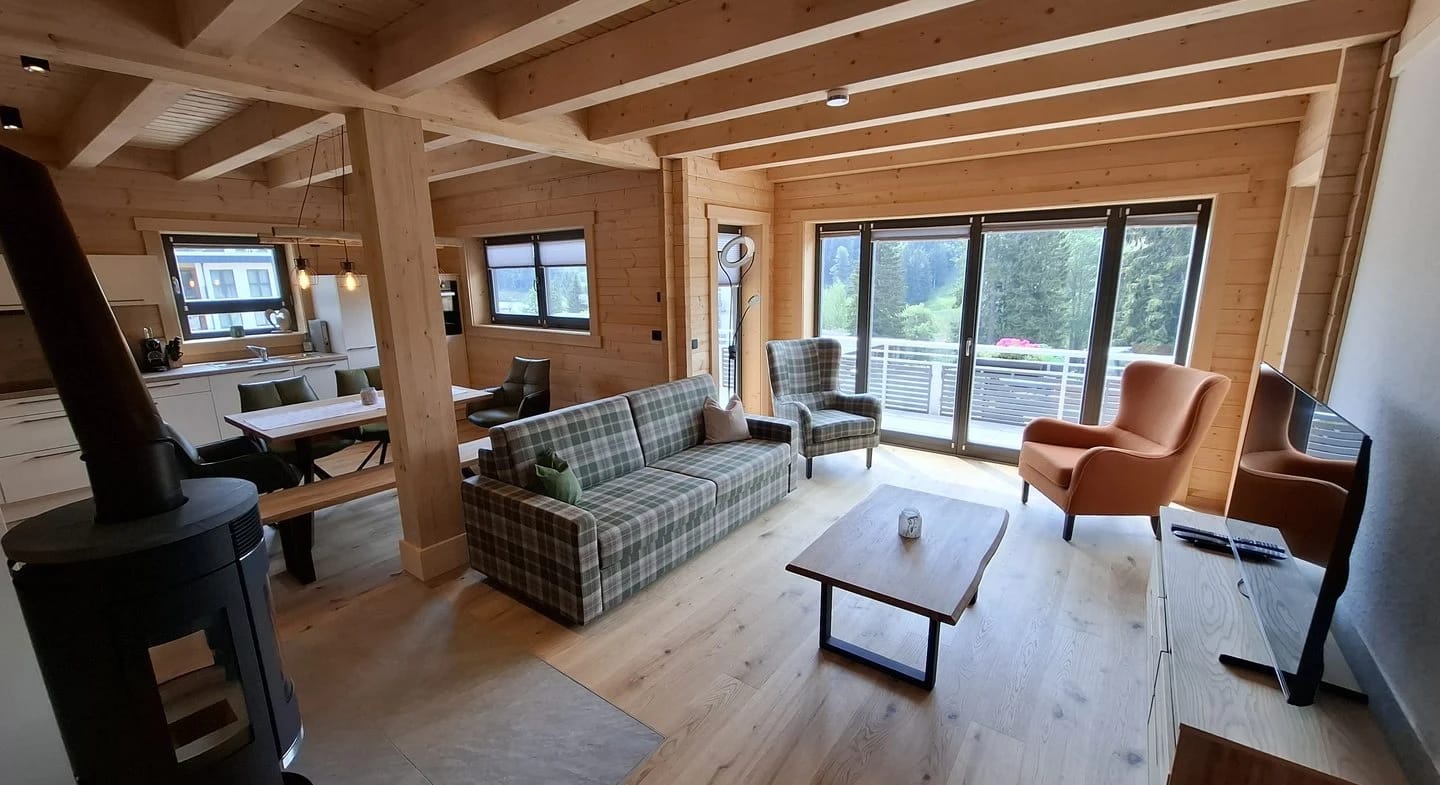 Wohnraum im Holzchalet mit Sofa, Sesseln, Kaminofen und Tür zur Terrasse