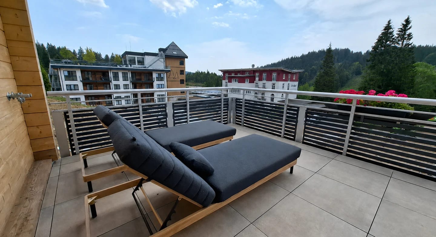 Terrasse mit zwei Sonnenliegen, im Hintergrund die Hotelgebäude und bewaldete Hänge