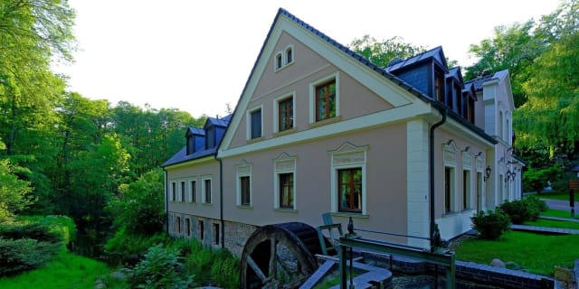 Historisches Mühlengebäude mit Wasserrad und hellem Putz, umgeben von Bäumen