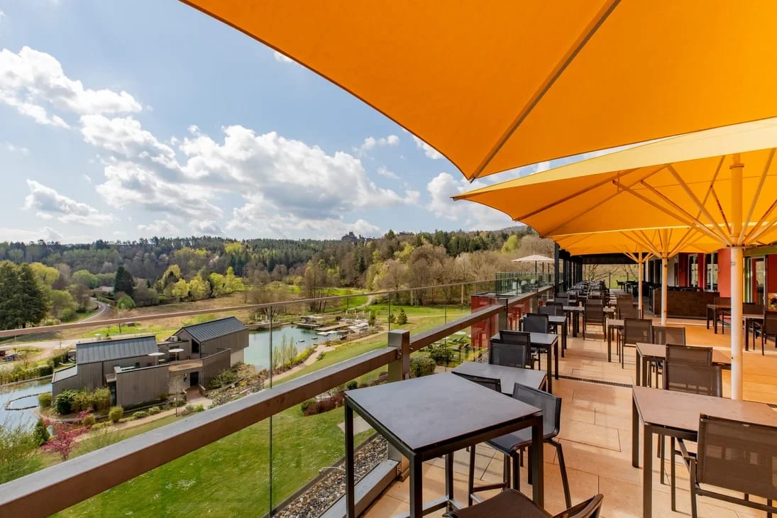 Sonnige Terrasse mit Tischen und Sonnenschirmen und Blick über das bewaldete Tal