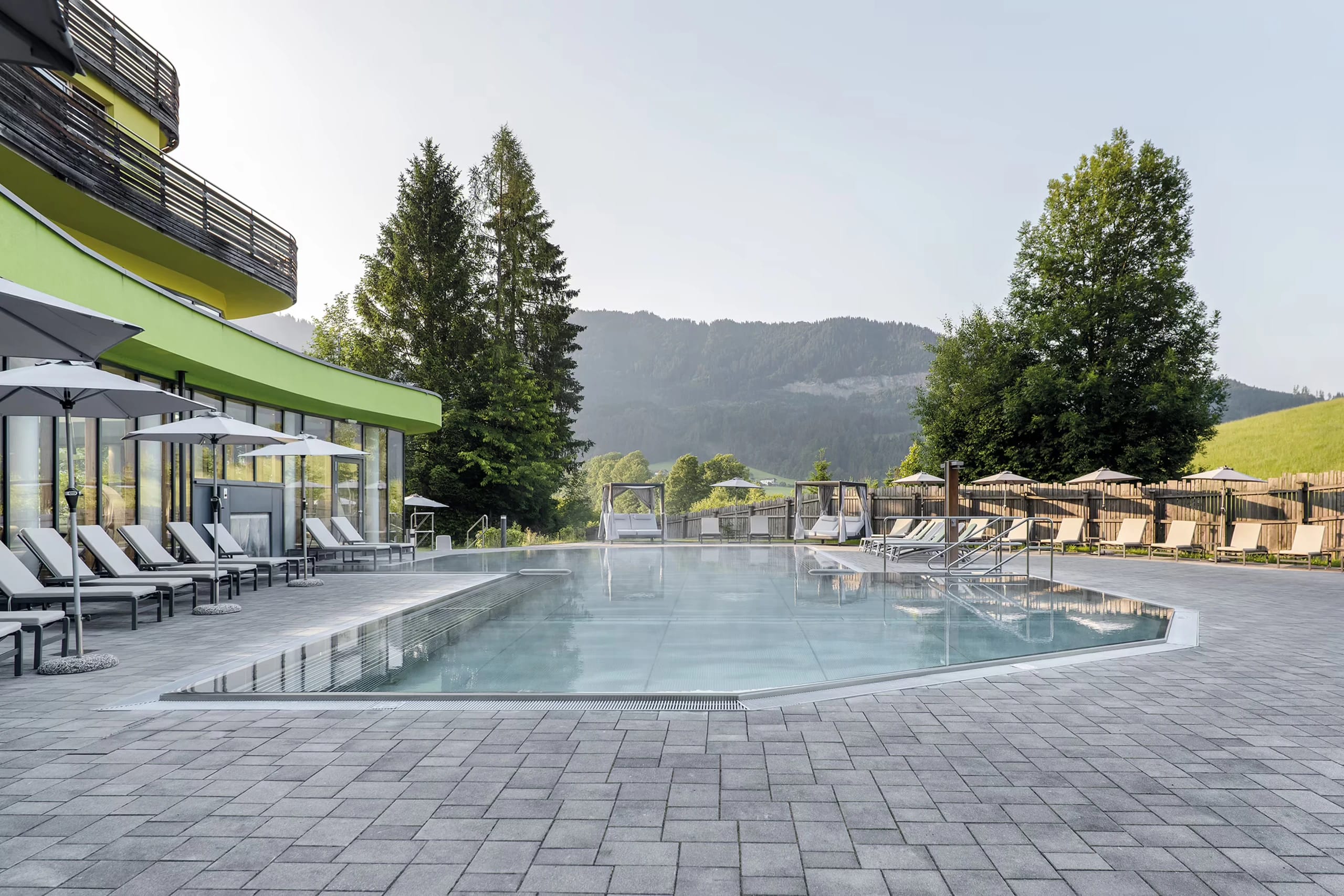 Großer Außenpool mit gepflasterter Terrasse, Sonnenliegen und Blick ins Grüne
