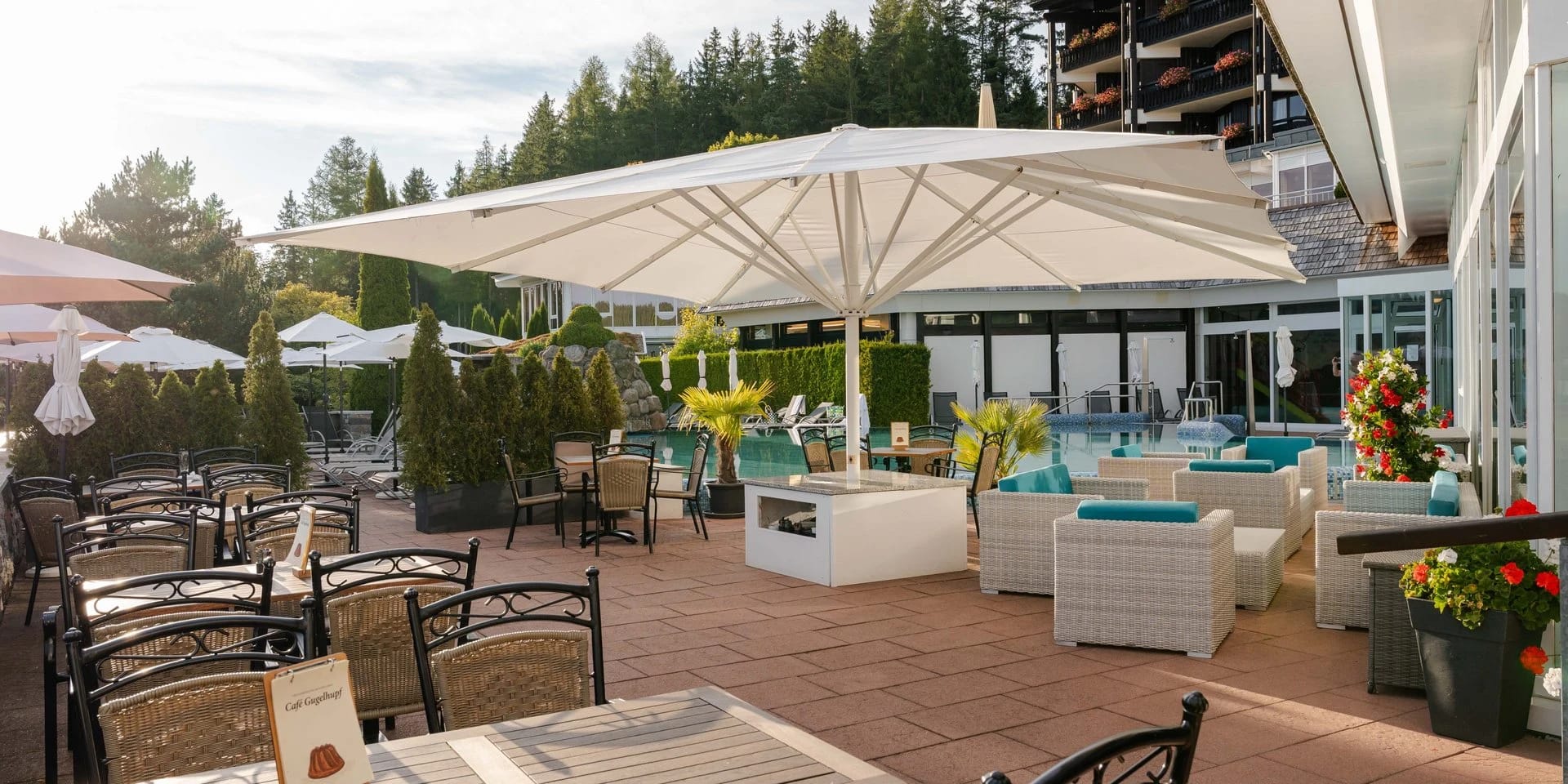 Sonnige Terrasse mit weißen Sonnenschirmen und Loungemöbeln vor dem Hotelgebäude mit Balkonen
