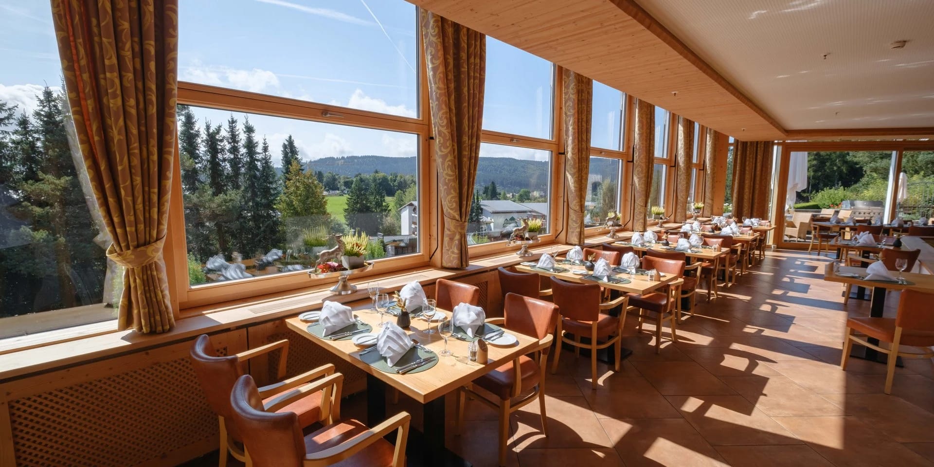 Heller Speisesaal mit Fensterfront, eingedeckten Tischen und Blick auf die bewaldeten Hügel