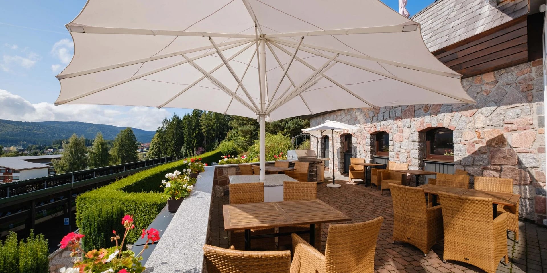 Sonnenterrasse mit großem weißem Sonnenschirm, Korbsesseln und Blick über die bewaldeten Hügel