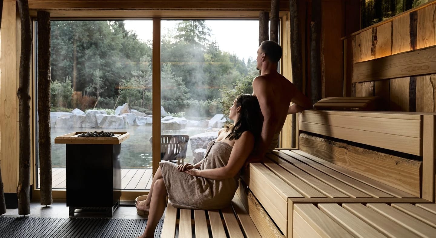 Sauna mit Saunaofen und raumhohem Fenster mit Blick in den Wald