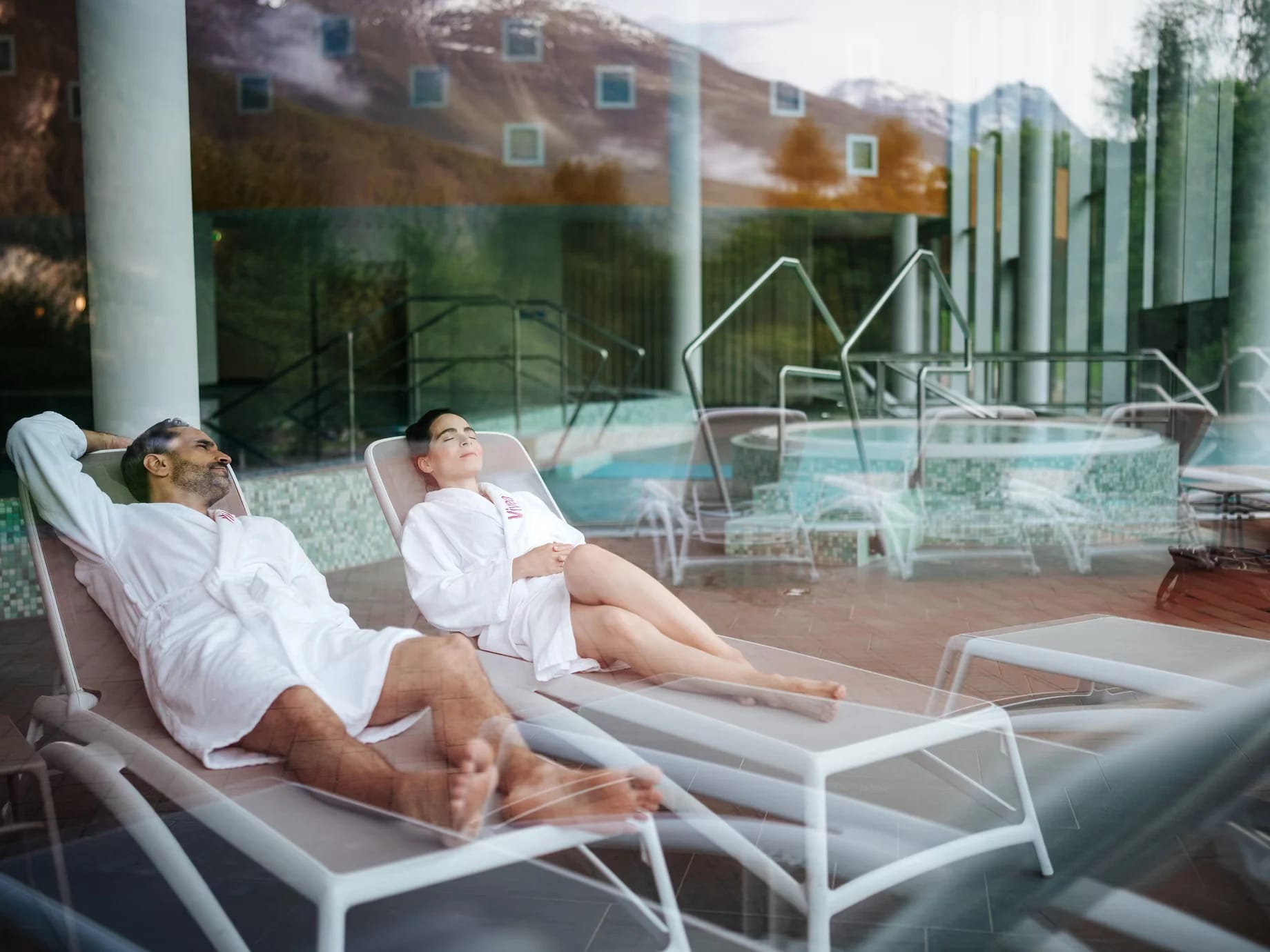 Hallenbad mit Relaxliegen hinter der Glasfront