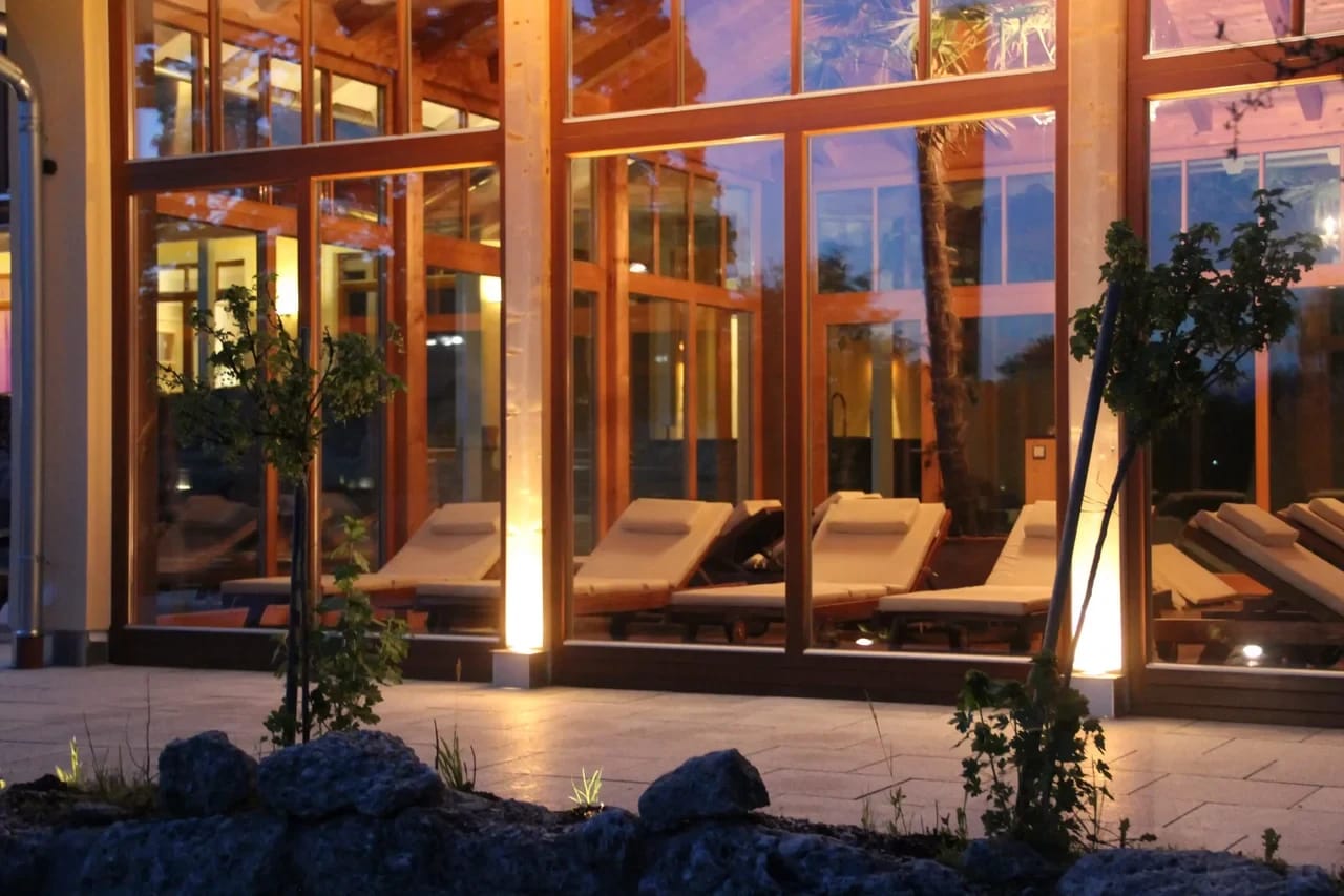 Beleuchtete Ruheliegen hinter der Glasfront des AlpenSpa in der Abenddämmerung