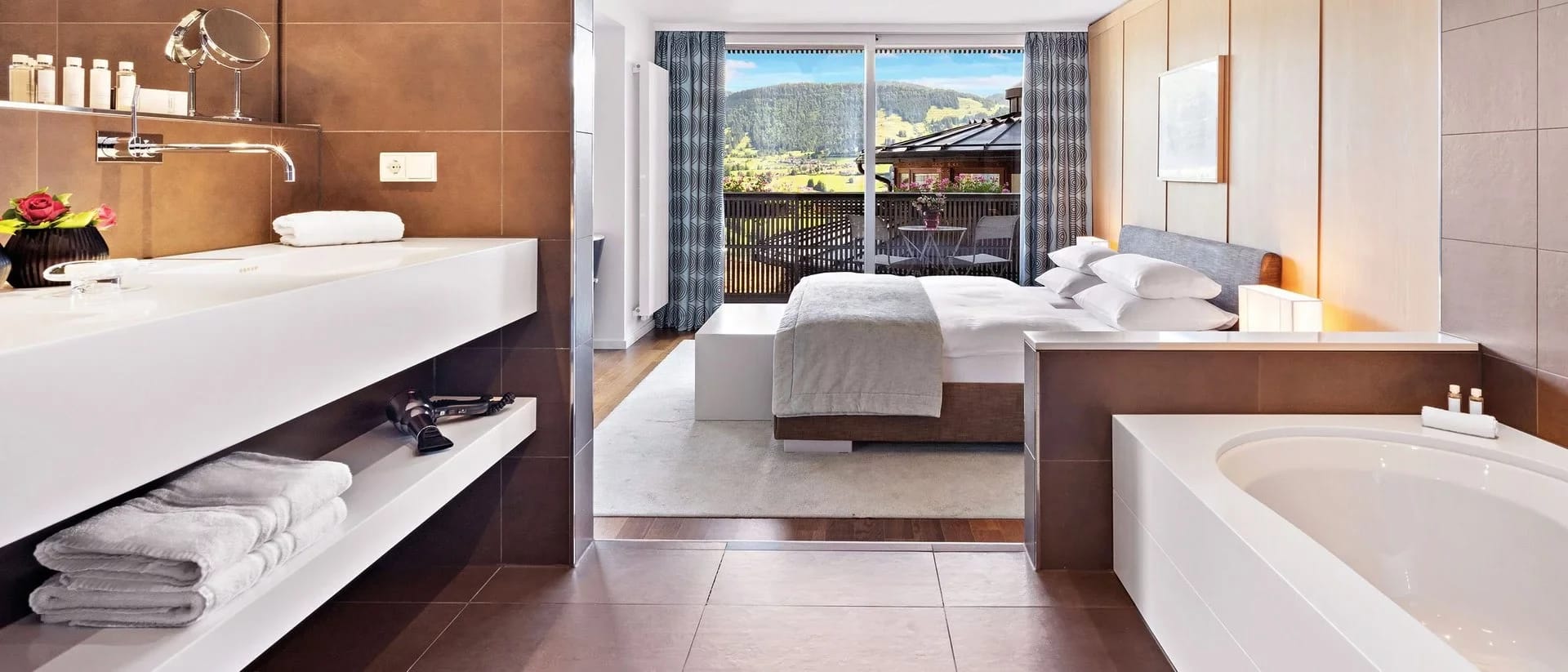 Badezimmer mit Doppelwaschtisch und Badewanne, offener Blick zum Schlafbereich mit Balkon