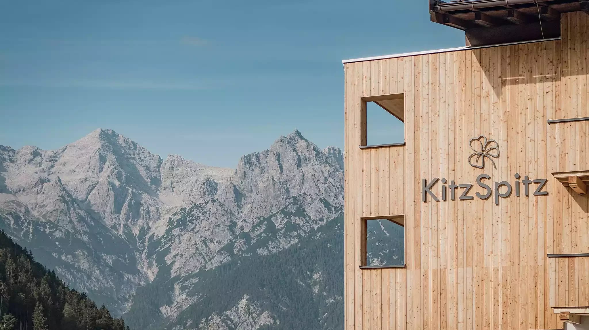 Holzfassade des Hauses mit KitzSpitz-Schriftzug und Bergpanorama