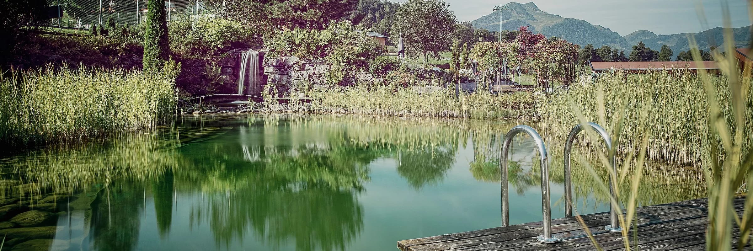 Naturbadeteich mit Wasserspiel und Blick auf die Berge