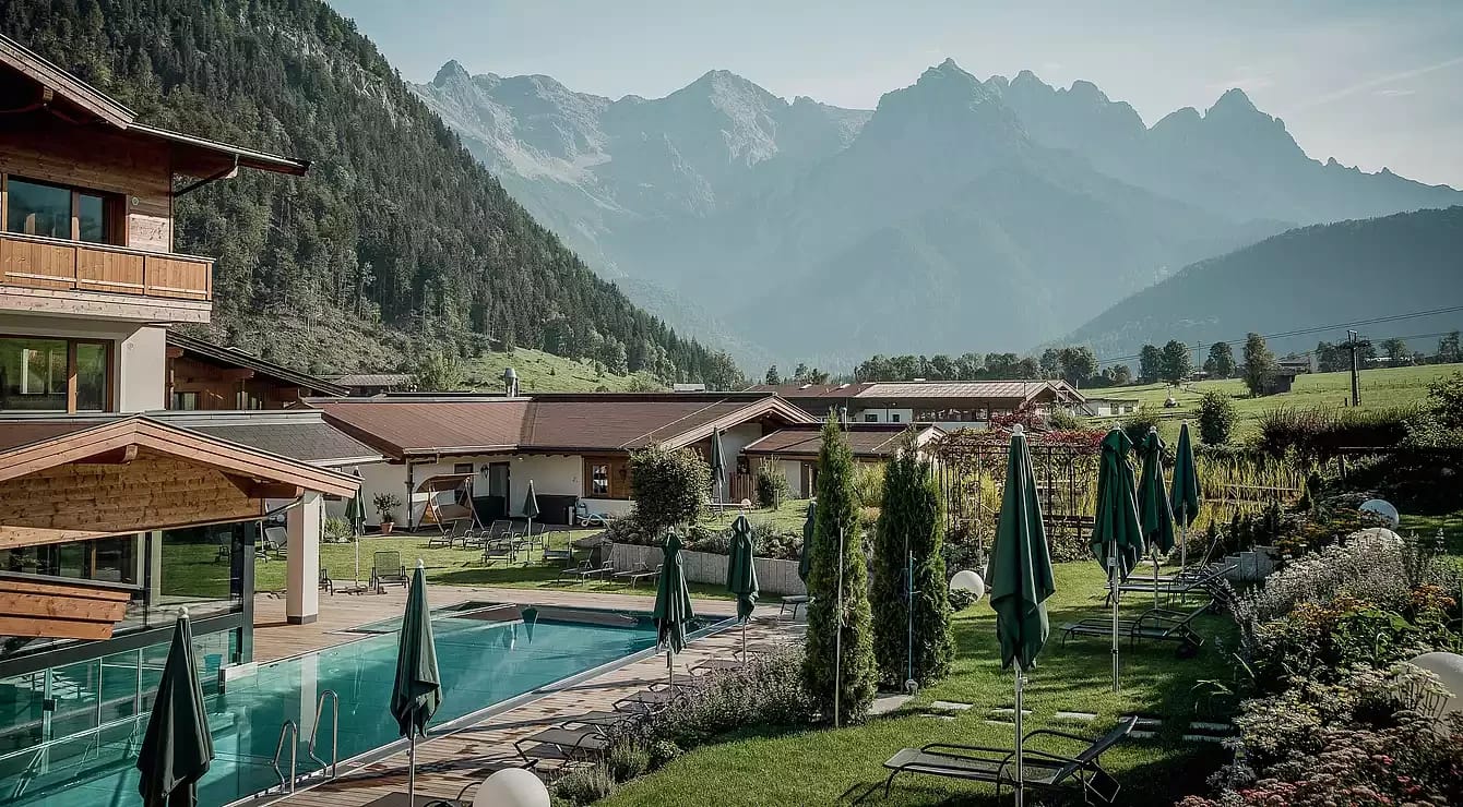 Wellnessgarten mit Pool und Hotelgebäude vor den Bergen
