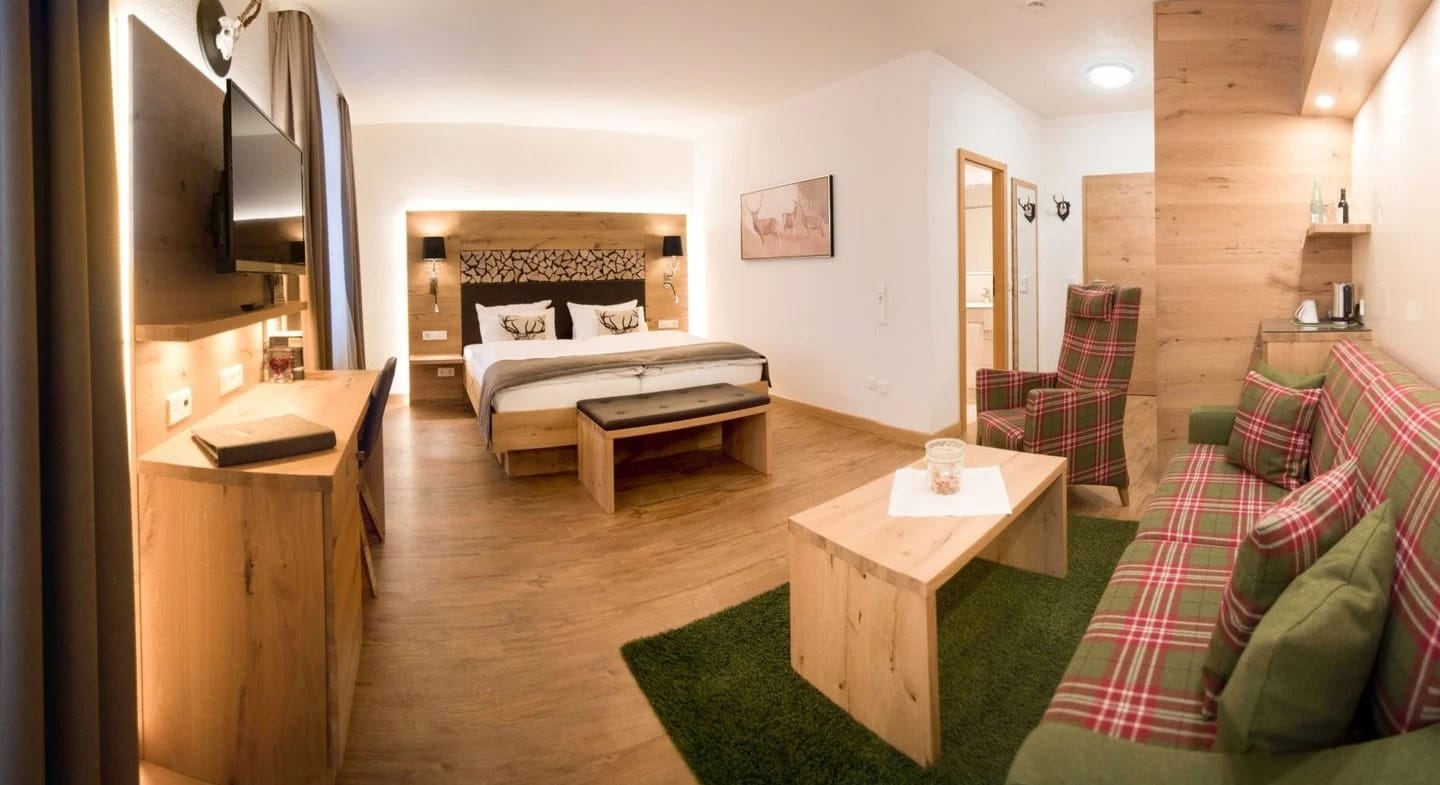 Juniorsuite mit Doppelbett, Sitzecke mit kariertem Sofa und Sessel auf hellem Holzboden