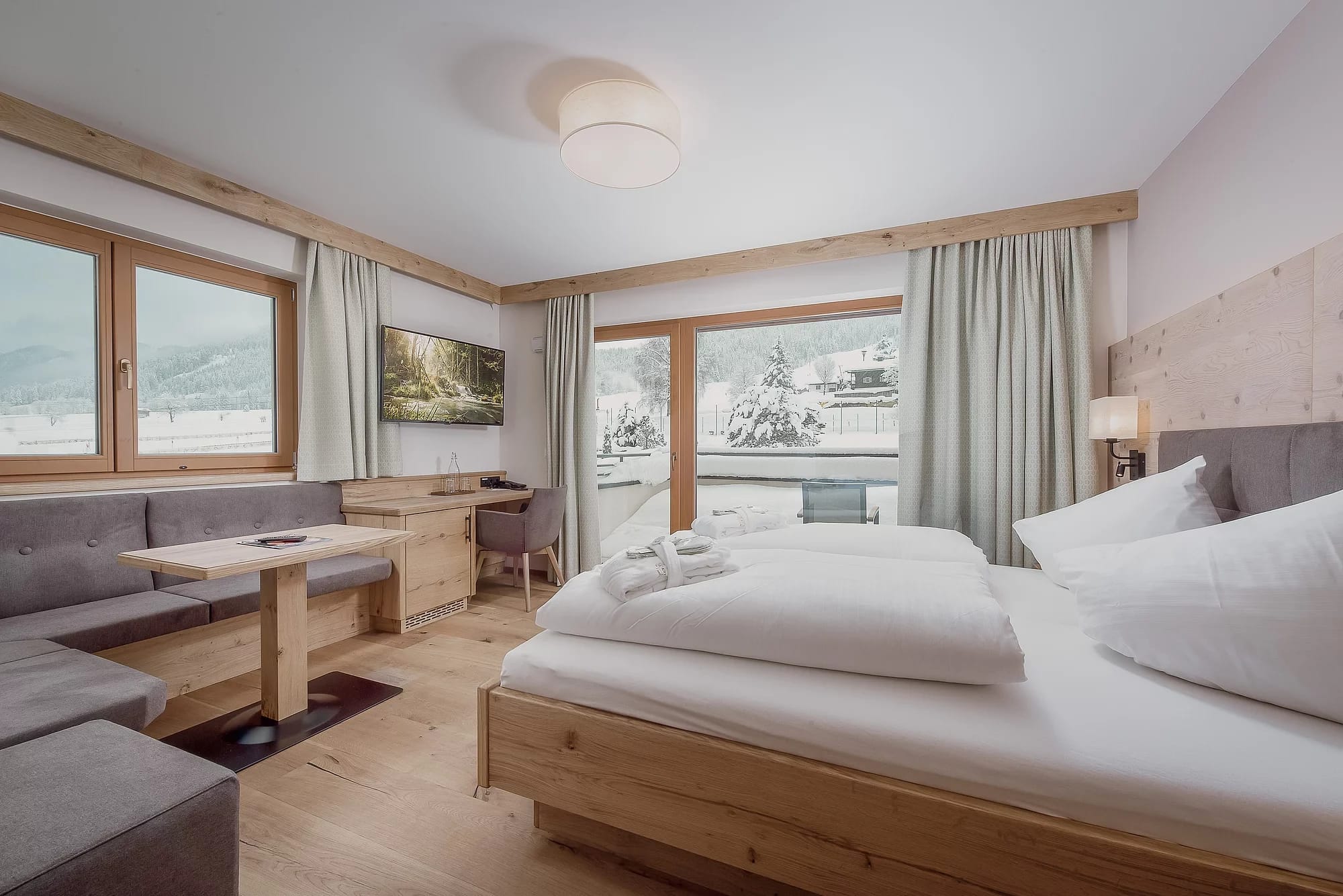 Helles Zimmer mit Doppelbett, Sitzecke und Fensterblick auf die verschneiten Berge