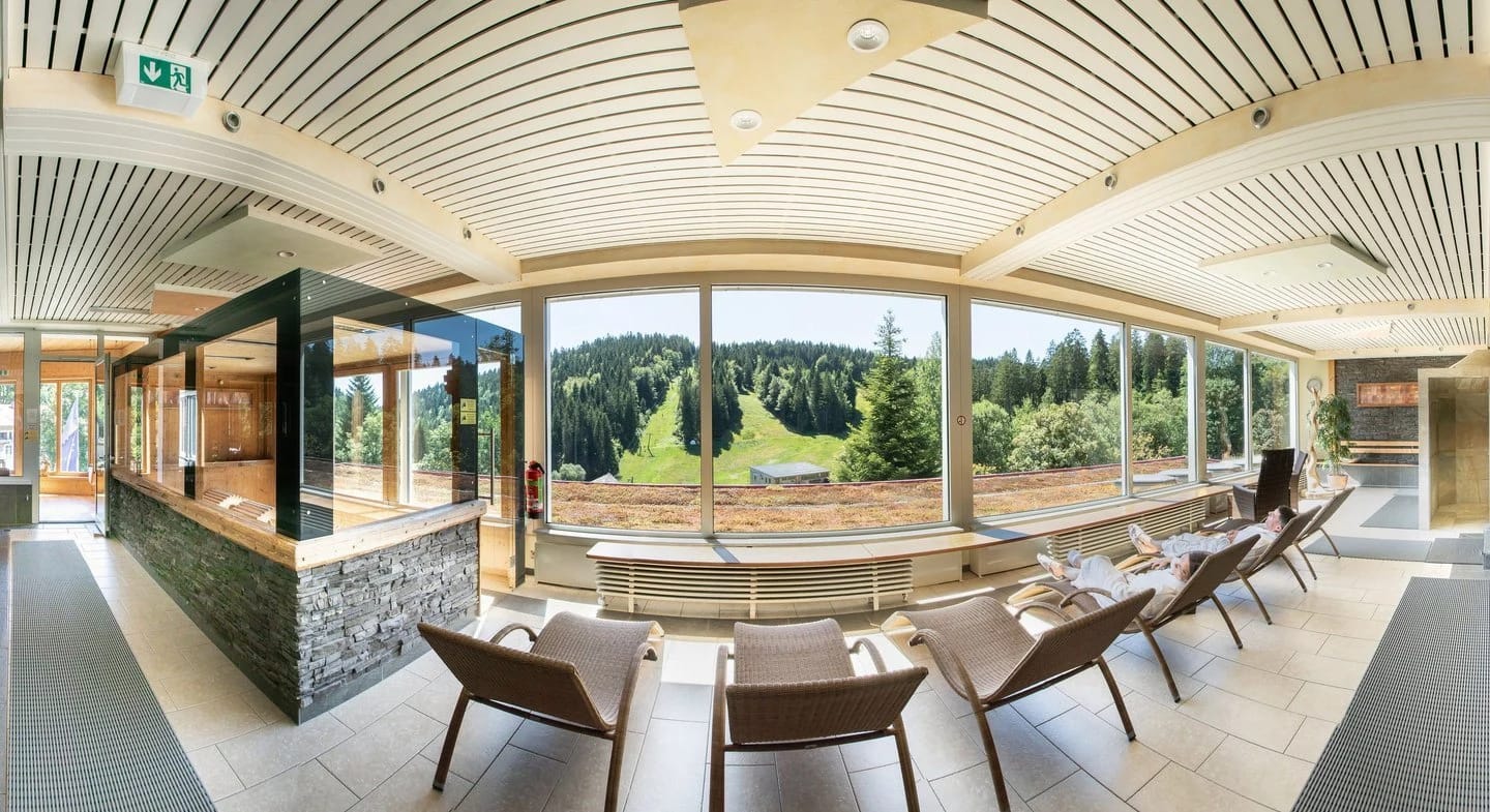 Panoramaraum mit Stuhlreihe vor der Fensterfront und Blick auf Wald und Wiese