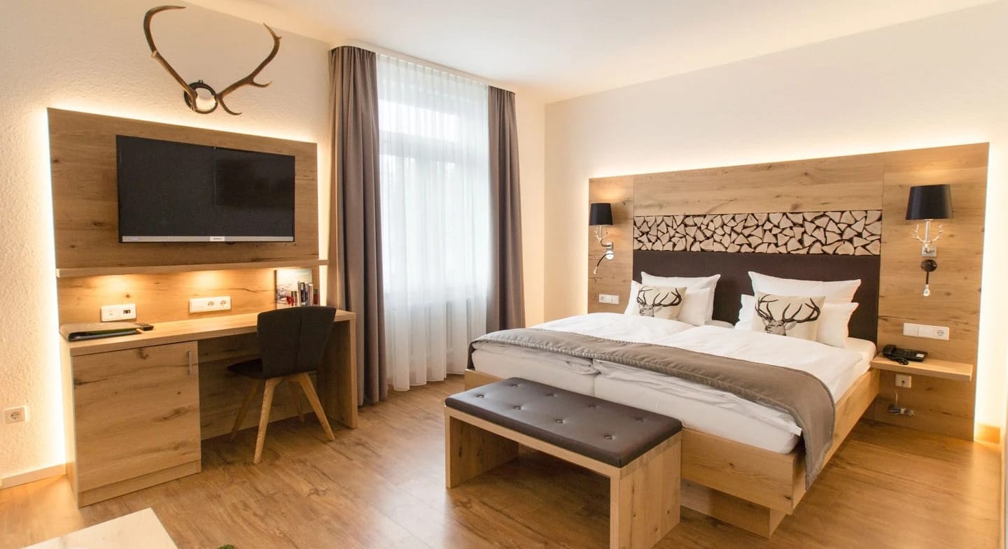 Hotelzimmer mit Doppelbett, Holzverkleidung, Schreibtisch und Geweih über dem Fernseher