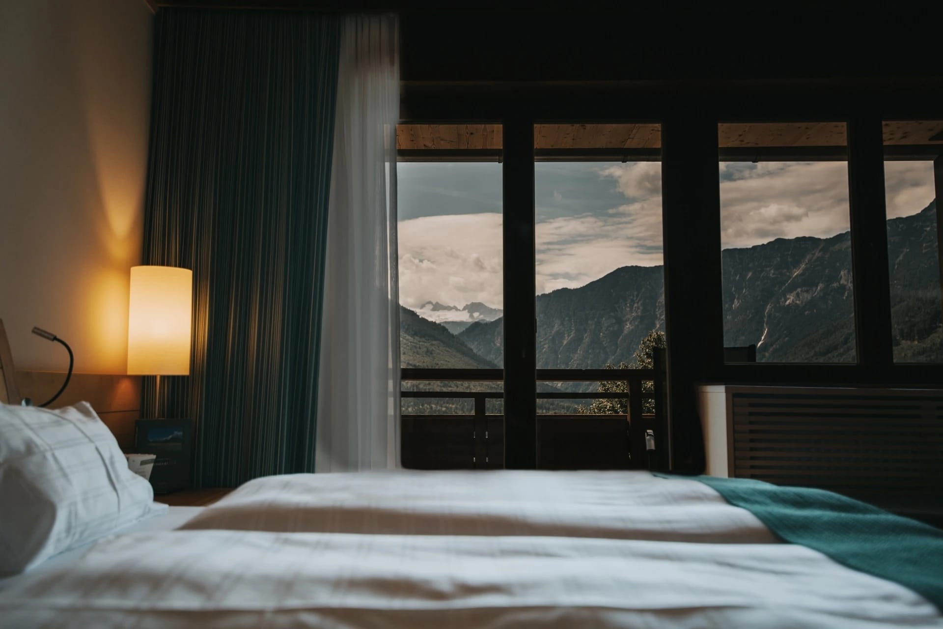 Bett mit weißer Bettwäsche und großem Fenster mit Bergblick im Zimmer Dachstein