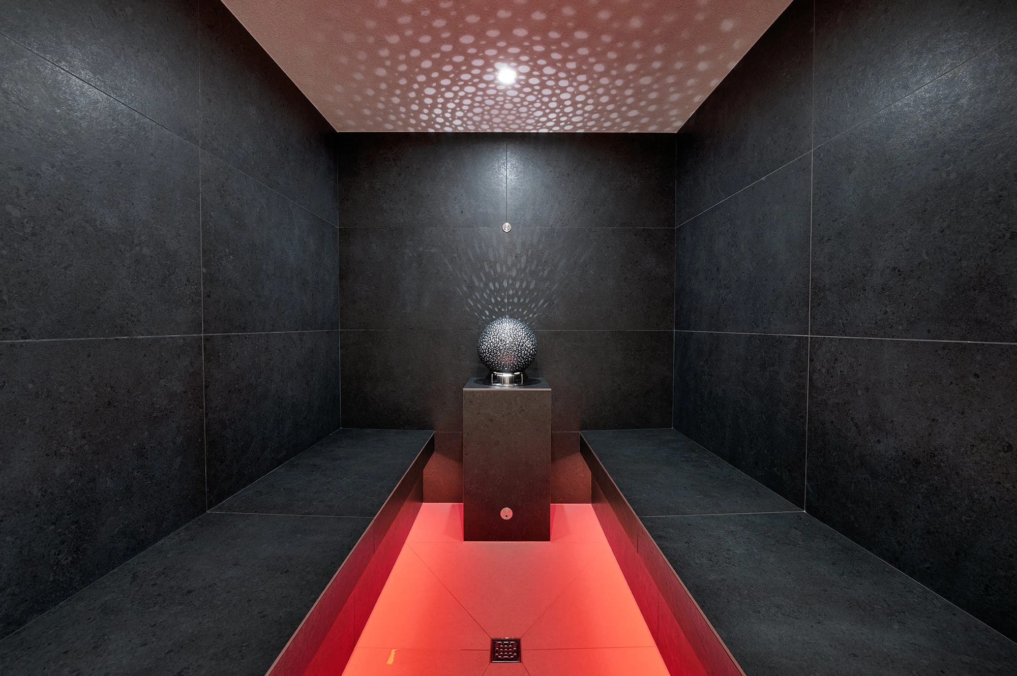Dampfbad mit dunklen Steinwänden, rot beleuchteter Wasserrinne und Lichtpunktdecke